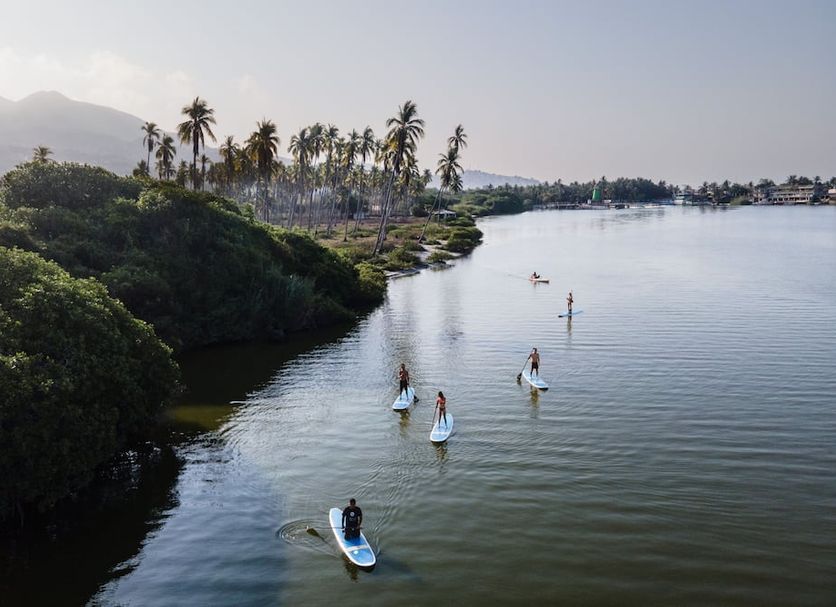 Baxar, Acapulco: people paddleboard on a calm lagoon beside palm trees and hills.