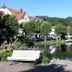 Landhaus Zu den Rothen Forellen in Ilsenburg: lakeside hotel with bench, trees and red-roofed buildings