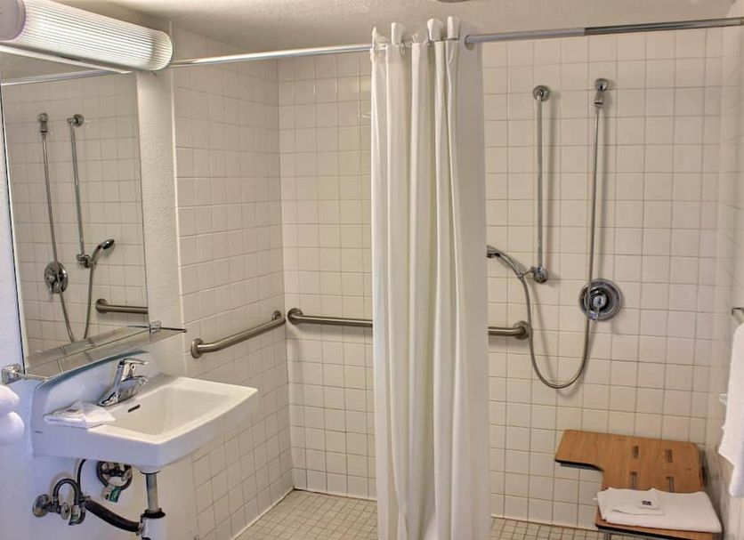 Motel 6 Coalinga East bathroom with roll-in shower, wall-mounted sink, grab bars and bench