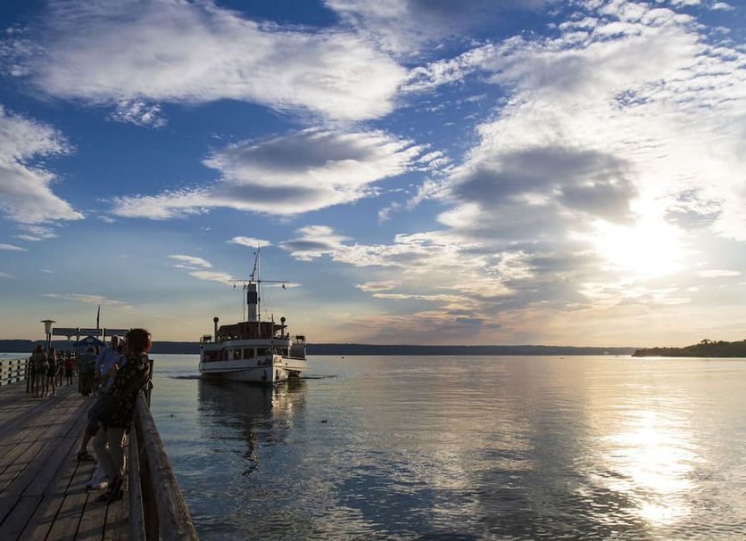 Seehof am Ammersee in Herrsching am Ammersee with lakeside pier, boat and sunset over calm water