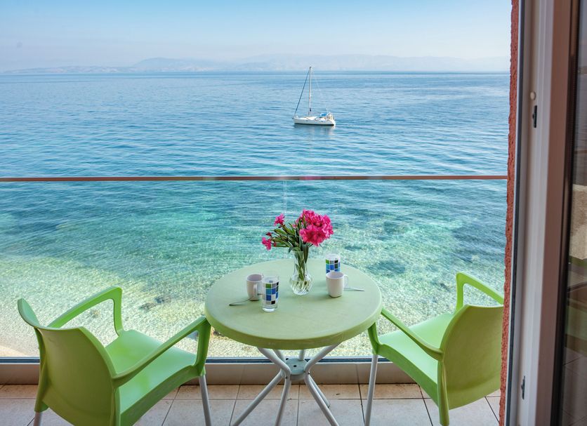 Corfu Maris Hotel in Benitses with balcony seating overlooking clear blue sea and a sailboat