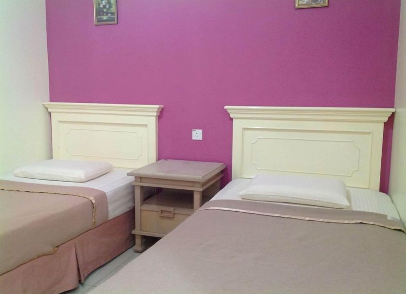 Hotel Morning Glory Kudat twin room with two single beds, bedside table, and pink accent wall
