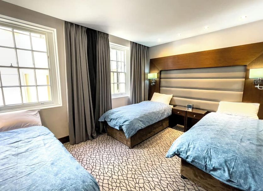 Lha Paddington Hostel London room with three single beds, large windows, curtains and padded headboard
