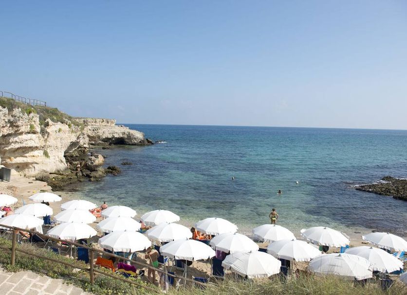 Corvino Resort in Monopoli with beach umbrellas beside a rocky seaside and clear blue water