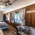 Hotel Lener in Mauls: wood-paneled guest room with bed, sitting chair, ceiling fan and windows with curtains.