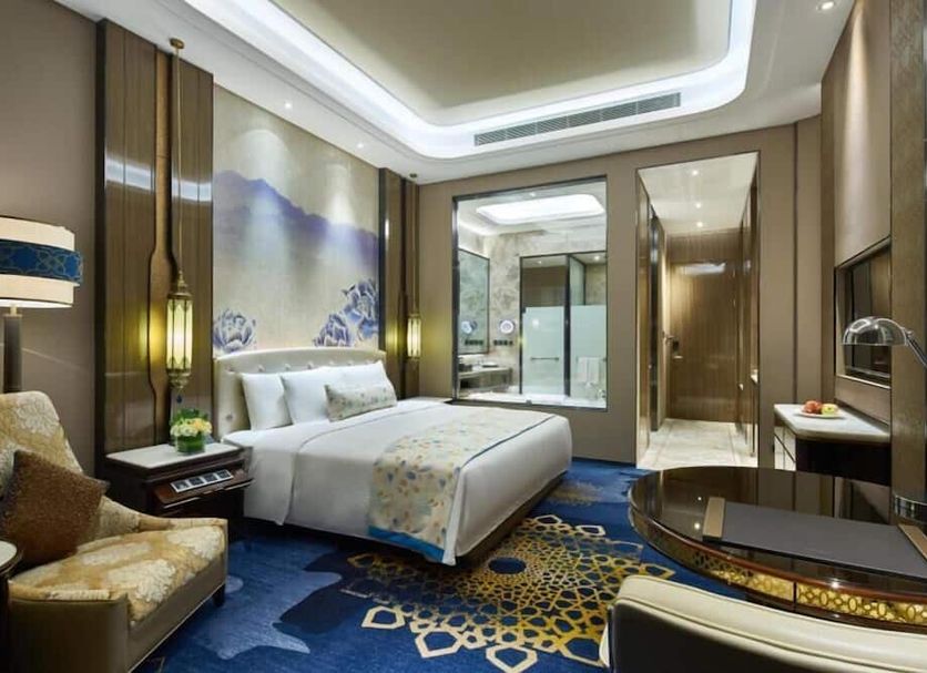Wanda Vista Urumqi guest room with king bed, blue patterned carpet, and marble bathroom in Ürümqi