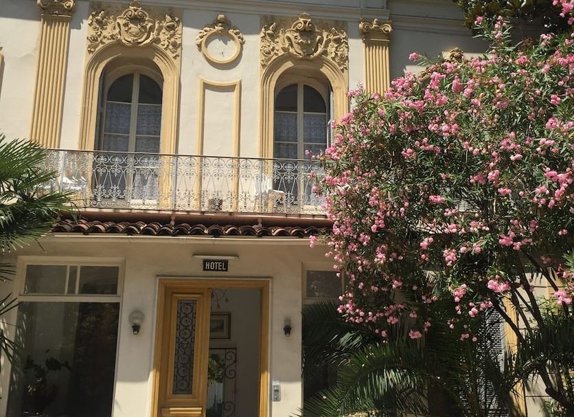 Hôtel Belle Meunière in Nice facade with ornate windows, balcony, and pink flowering tree