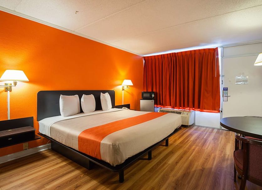 Motel 6 Tifton Ga guest room with king bed, orange accent wall, wood flooring, and red curtains
