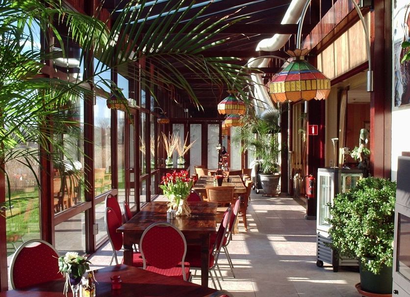 Hotel Den Helder in Den Helder features a bright glass-walled dining area with red chairs and potted plants.