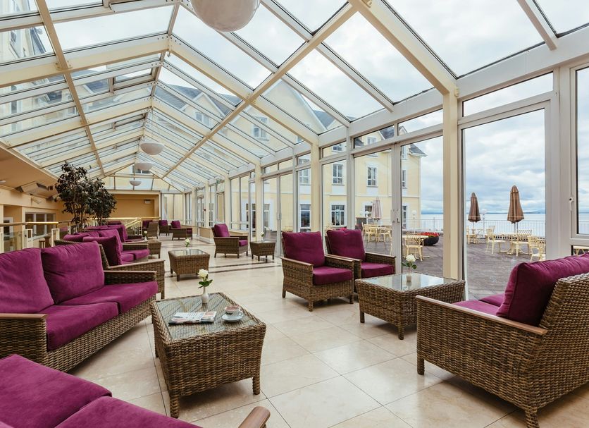 Galway Bay Hotel, Galway: glass-enclosed lounge with wicker seating and purple cushions overlooking the sea