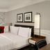 The Dilly London guest room with king bed, red armchair, floor lamp, and large window