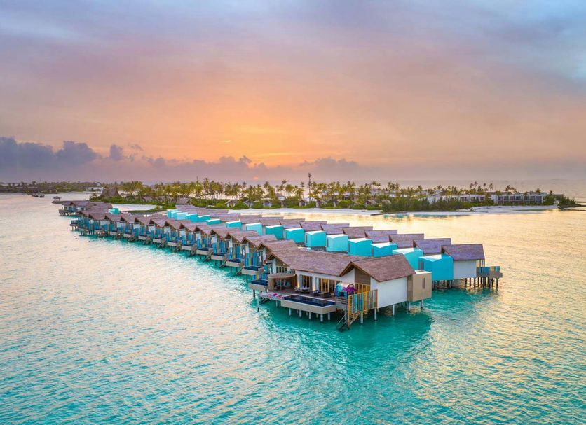 Hard Rock Hotel Maldives in Malé with overwater villas above turquoise water at sunset