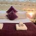 Dolgun Uchaf Guesthouse in Dolgellau: a made bed with purple cushions, rolled towels, and bedside lamp
