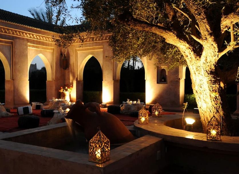 La Maison des Oliviers in Marrakech, lit courtyard with arched openings, seating, and a large olive tree