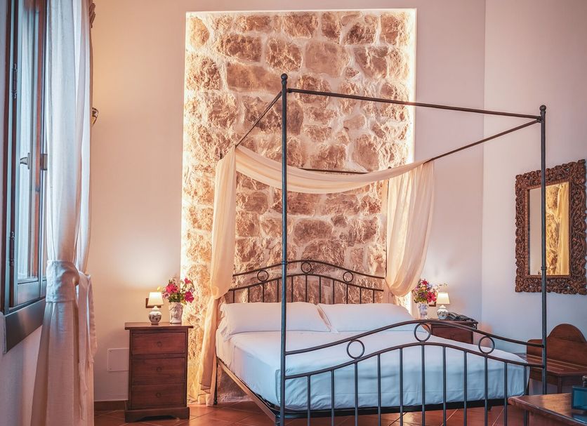 Hotel La Corte Del Sole in Noto: four-poster bed in a rustic room with stone accent wall and terracotta tile floor