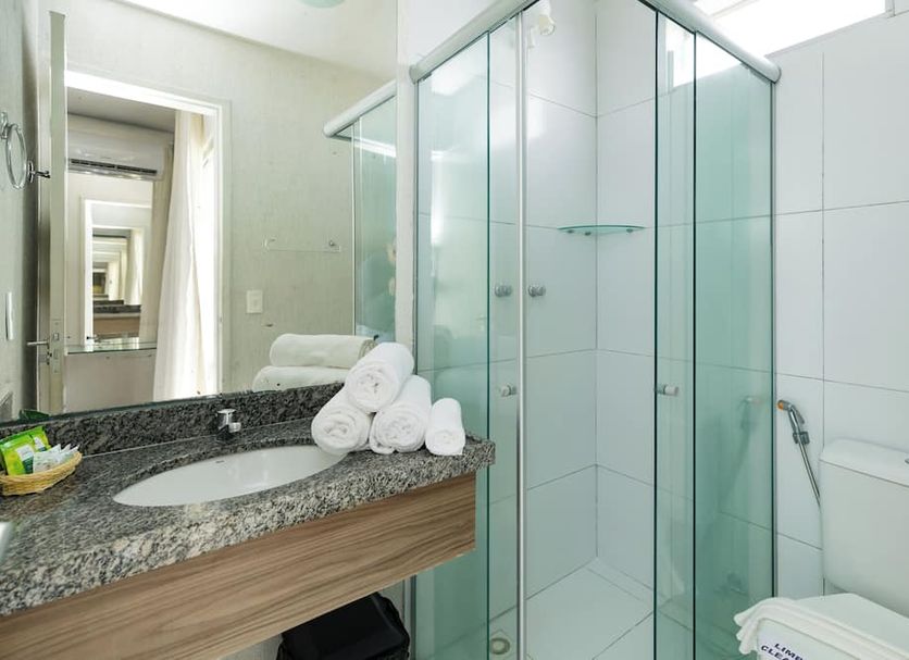 El Aram Ponta Negra bathroom in Natal with glass shower, granite vanity, and neatly rolled towels