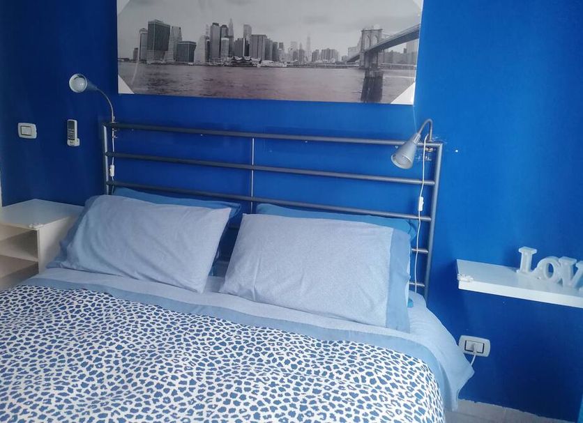 Travel And Living, Trani: blue guest room with metal bed frame, patterned bedding, and city wall art