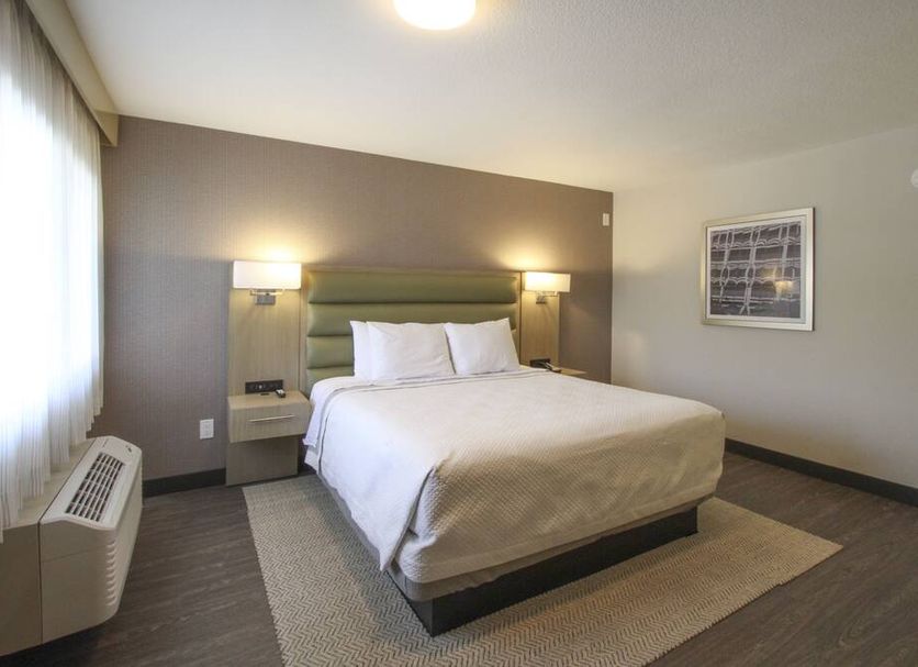 Greentree Pasadena Inn guest room with queen bed, bedside lamps, window air conditioner and framed wall art in Pasadena