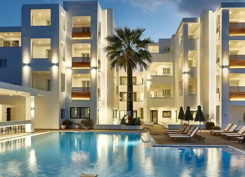 Arminda Hotel & Spa in Hersonissos with illuminated pool, palm tree and lounge chairs at dusk