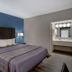 Motel 6 Burlington Nc guest room with king bed, blue accent wall, bedside lamps and vanity area in Burlington