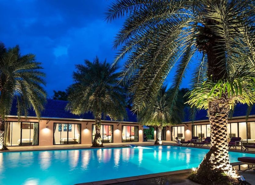 Ma Maison Boutique Hotel in Choeng Thale, Phuket, with a lit outdoor pool surrounded by palm trees at dusk
