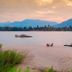 The River Resort in Champasak with a sandy riverbank, longboat, and mountain views at sunset