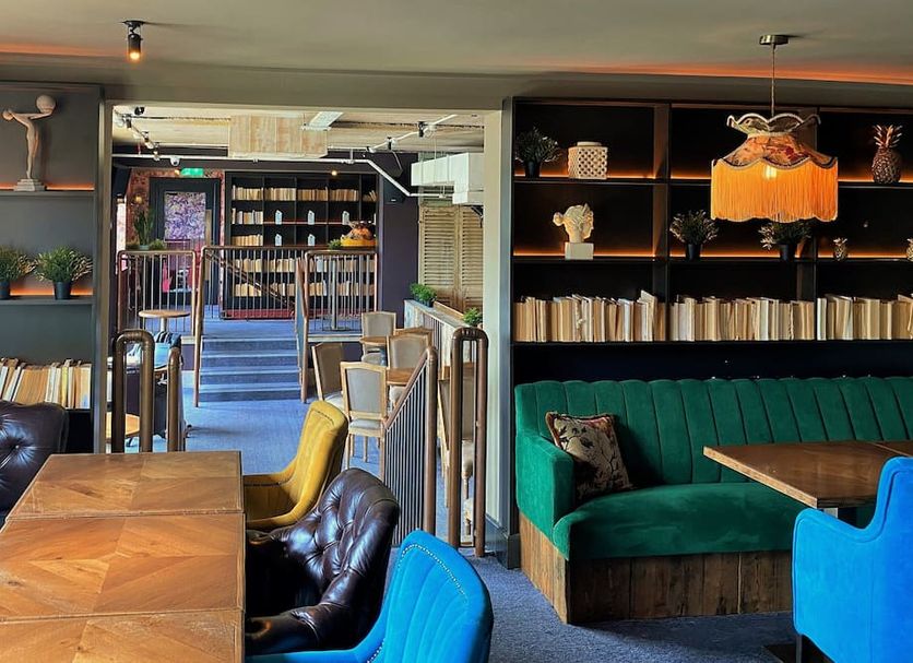 House Belfast Hotel in Belfast lounge with green velvet sofa, blue chairs, wooden tables and bookshelf wall
