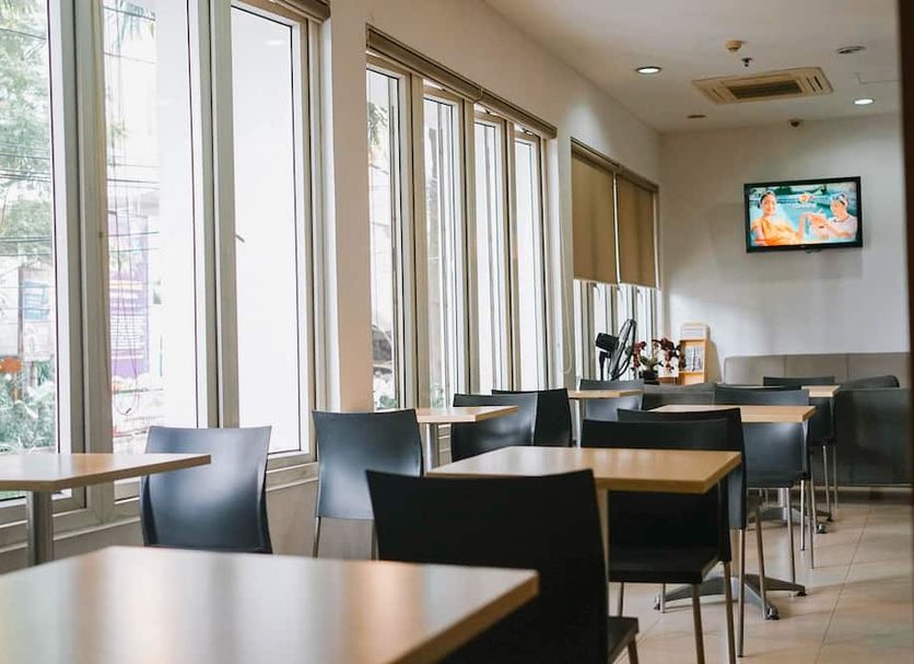 M Hotel Jakarta breakfast area with tables, black chairs, large windows and wall-mounted TV