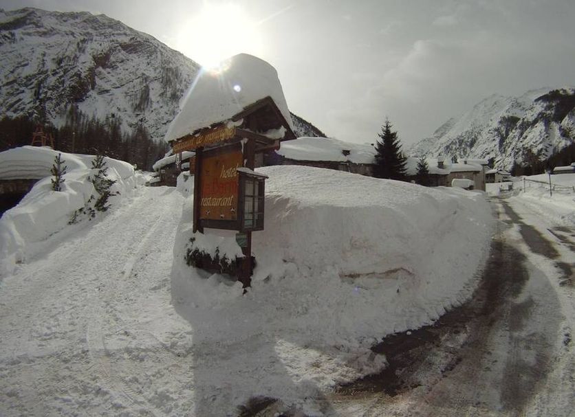 Hotel Restaurant La Barme in Cogne, snowy mountain road with sunlit alpine peaks and a signboard