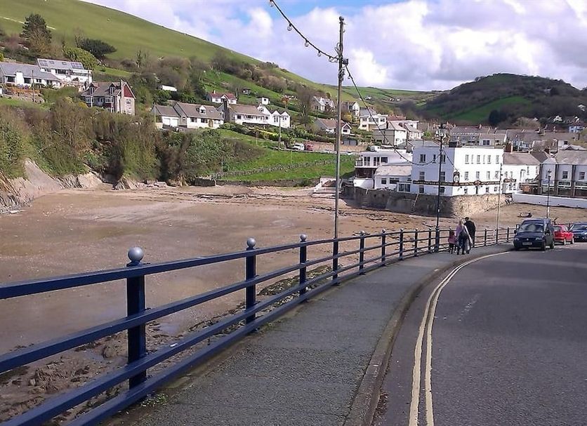 Saffron House, Combe Martin: riverfront road with railings, village buildings, hills and parked cars