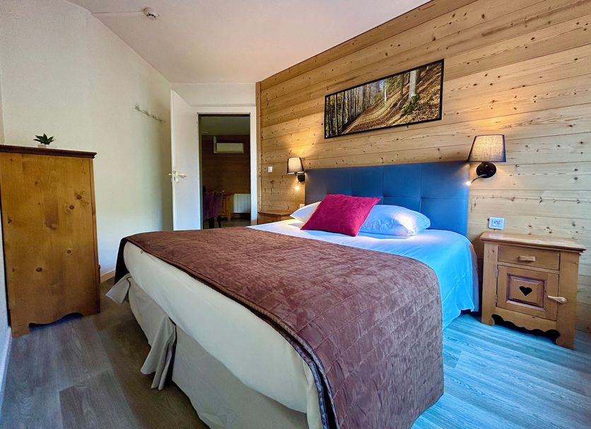 Résidence Côté Chalet in Thonon-les-Bains: cozy bedroom with wood-paneled wall, bed, and bedside lamps