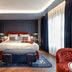 Seda Club Hotel in Granada guest room with king bed, blue bench, patterned rug and floor-to-ceiling curtains