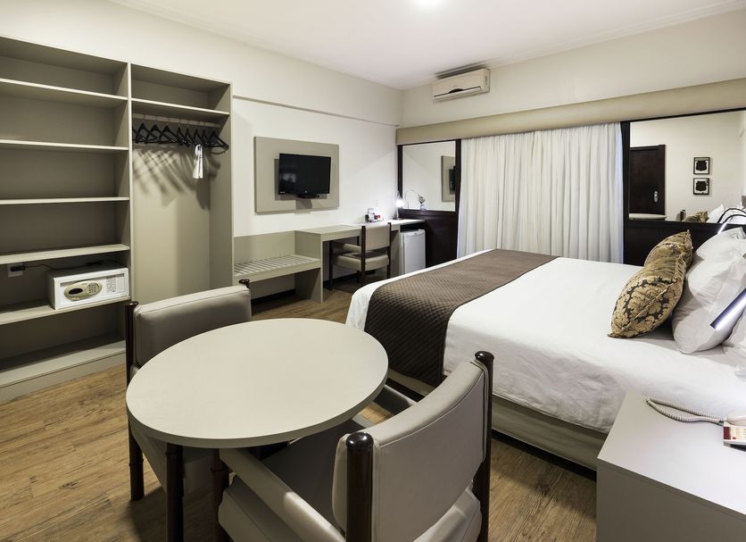 Plaza Blumenau Hotel room in Blumenau with bed, round table, desk, closet and wall-mounted TV