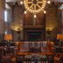Hotel Emma San Antonio lobby with leather seating, brick walls, and a large wagon-wheel chandelier