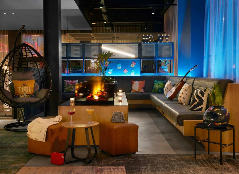 Moxy Milton Keynes lounge with fireplace, hanging chair, sofa seating and city-view windows
