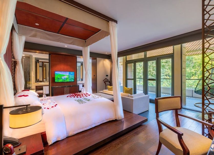 Millennium Resort Hangzhou bedroom with canopy bed, TV, seating area and forest-view windows
