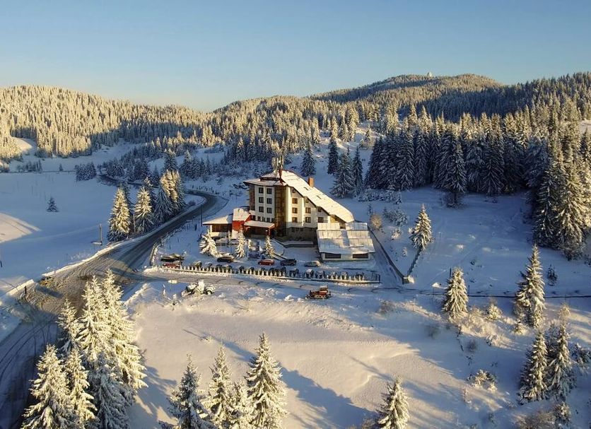 Hotel Coop Rozhen in Pamporovo surrounded by snowy mountains and pine trees, aerial view
