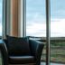 Afternoon Cottages in Hella: black armchair by floor-to-ceiling windows with a scenic green landscape view