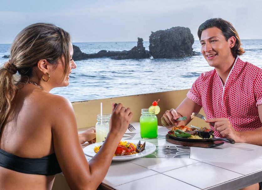 Hotel Roca Sunzal in El Sunzal: couple dining at a seaside table with ocean and rocks behind them