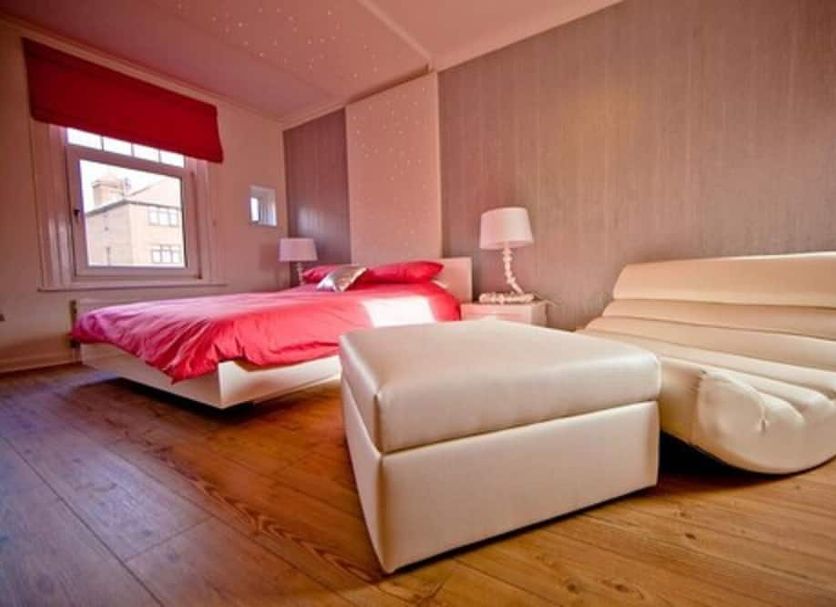 G Boutique Hotel in Portsmouth guest room with red bed, ottoman, curved chair, and wood flooring