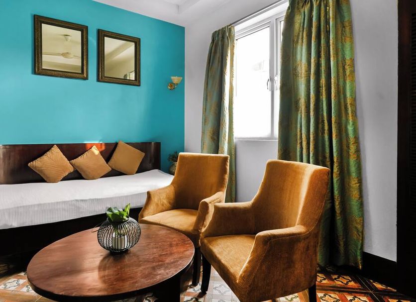 Hotel Ajanta New Delhi guest room with teal wall, sofa bed, two chairs and round coffee table