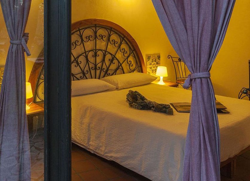 Villa dei Papiri in Siracusa bedroom with wrought-iron headboard and purple curtains by a glass door