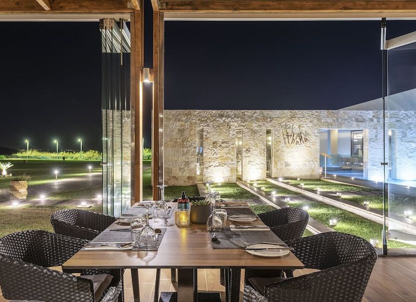Astir Odysseus Kos Resort & Spa in Tigaki: outdoor dining table beside a lit stone wall and garden at night