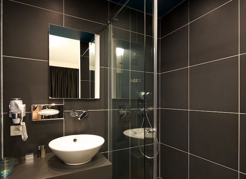 Le Nexhotel Tarbes modern bathroom with vessel sink, mirror, glass shower and dark tile walls