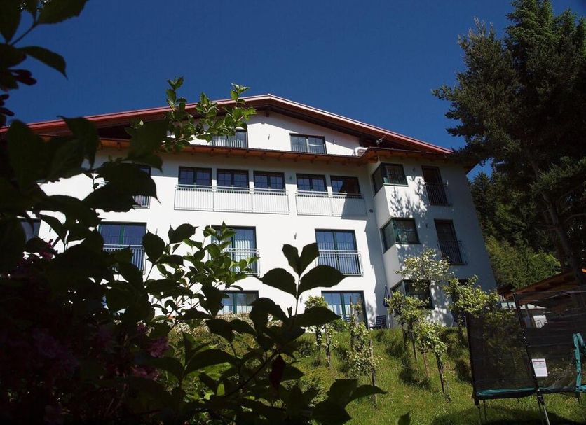 Hotel Planaiblick in Schladming, white alpine hotel viewed through greenery under a clear blue sky