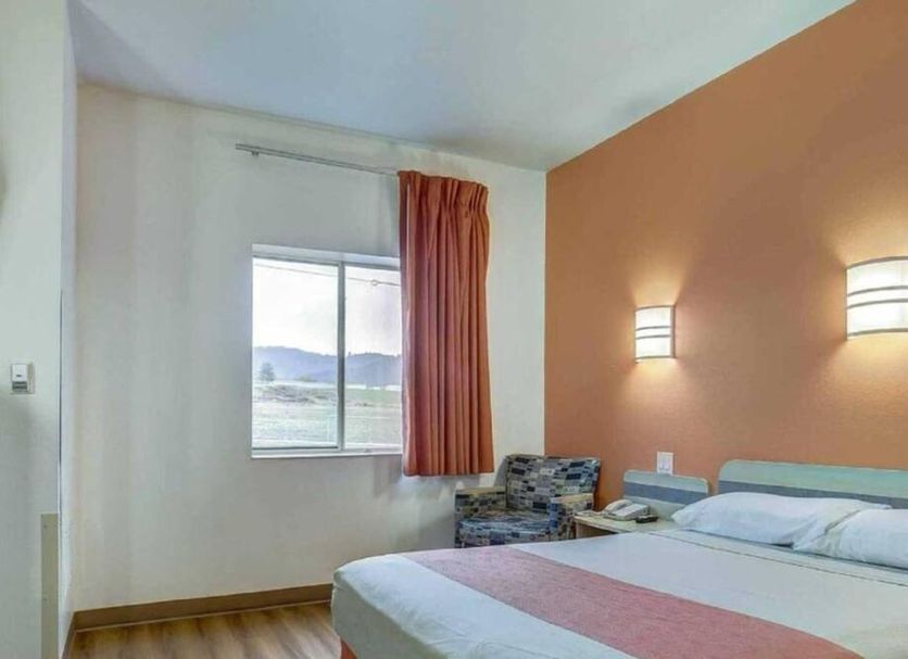 Motel 6 Roseburg room with queen bed, window view, chair, and wall sconces in Roseburg