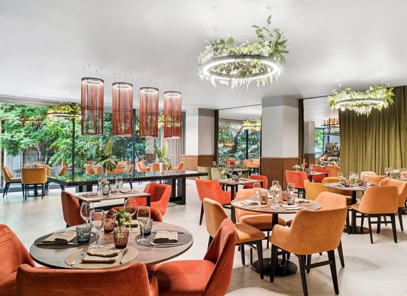 NH Collection Mexico City Reforma restaurant with orange chairs, set tables, and lush hanging greenery in Mexico City