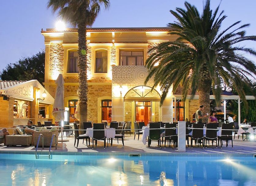 Grecian Castle Chios in Chios with lit poolside terrace and palm trees at dusk