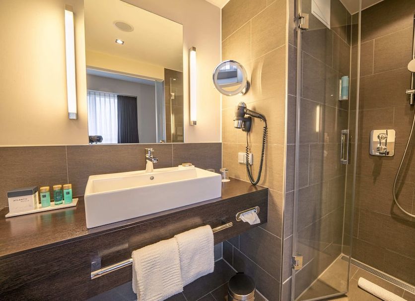 Atlantic Hotel Lübeck bathroom with vessel sink, mirror lights, and glass walk-in shower in Lübeck