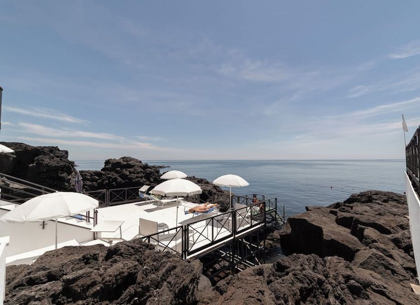 Hotel Nettuno in Catania with a seaside terrace, white umbrellas, and rocky shoreline views